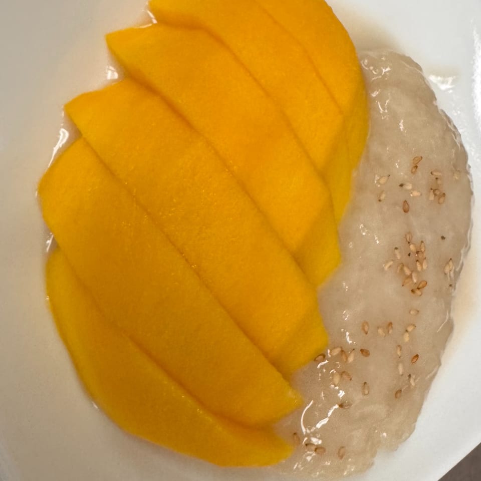 Mango sticky rice dessert with sliced mango and sesame seeds on a white plate.
